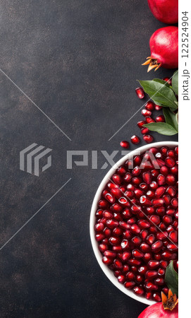 bowl of pomegranate seeds with fresh fruit and leaves on dark background 122524904