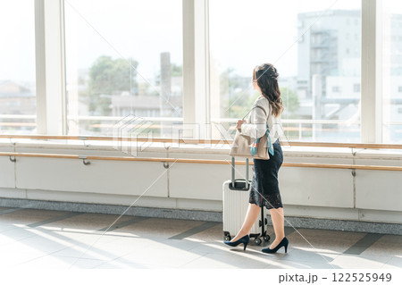 スーツケースを持って空港・駅・ターミナルのロビー・通路を歩く若いビジネスウーマン スーツケースを持って空港・駅・ターミナルのロビー・通路を歩く若いビジネスウーマン 122525949