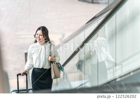 駅でエスカレーターに乗るスーツケースを持った出張・旅行帰りの女性・ビジネスウーマン 駅でエスカレーターに乗るスーツケースを持った出張・旅行帰りの女性・ビジネスウーマン 122526202