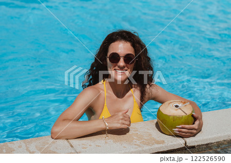 young beautiful happy girl in sunglasses with a drinking coconut is relaxing in swimming pool at a hotel in a resort in summer on vacation young beautiful happy girl in sunglasses with a drinking coconut is relaxing in swimming pool at a hotel in a resort in summer on vacation 122526590