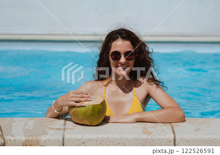 portrait of beautiful young woman in sunglasses with a drinking coconut is relaxing in swimming pool at hotel in resort in summer on vacation 122526591