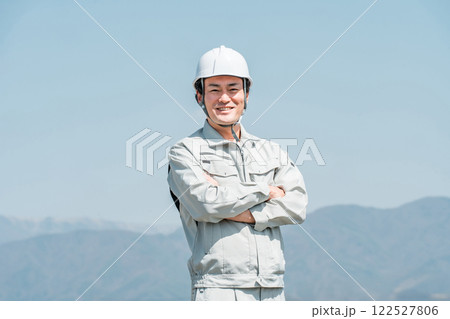 青空の下に立つヘルメットを被った作業着姿の男性(建築・土木・建設) 青空の下に立つヘルメットを被った作業着姿の男性(建築・土木・建設) 122527806