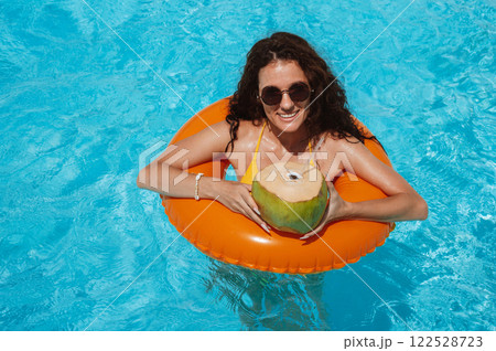 young beautiful girl in sunglasses with coconut rests in an inflatable circle in pool at a hotel on vacation at resort in summer holidays young beautiful girl in sunglasses with coconut rests in an inflatable circle in pool at a hotel on vacation at resort in summer holidays 122528723