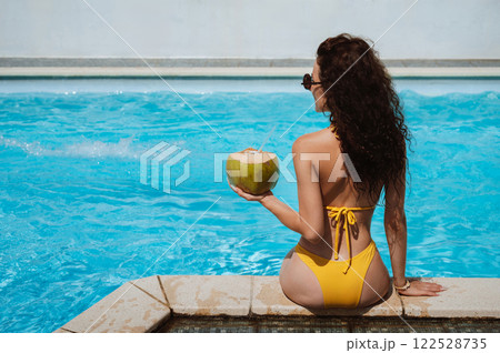 back of young sexy beautiful woman with coconut relaxing by swimming pool at hotel in a resort in summer on vacation 122528735