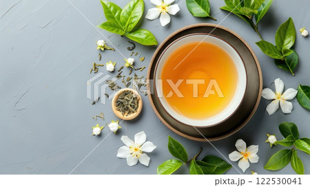 A cup of green tea with jasmine flowers and leaves on a gray background. A cup of green tea with jasmine flowers and leaves on a gray background. 122530041