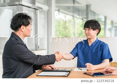 握手する医療機器メーカーのビジネスマンとスクラブ姿の医師 握手する医療機器メーカーのビジネスマンとスクラブ姿の医師 122530218