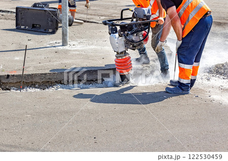 Construction workers repair pavement with heavy machinery at a busy urban site 122530459
