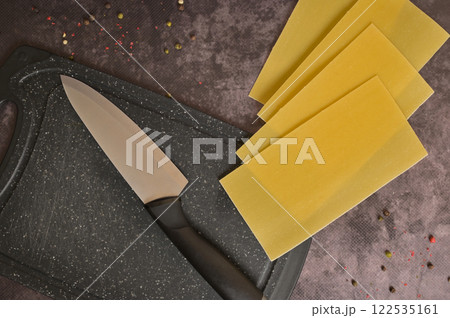 Top view knife and lasagne pasta sheets on a black kitchen cutting board. Black background. Homemade lasagna cooking preparation Top view knife and lasagne pasta sheets on a black kitchen cutting board. Black background. Homemade lasagna cooking preparation 122535161