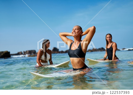 Three women sit on surfboards in blue ocean water. Smiling, relaxed. Warm sunny day. Ideal spot for surfing camp. Learn skills, enjoy waves. Perfect for school instructors teaching beginners. Three women sit on surfboards in blue ocean water. Smiling, relaxed. Warm sunny day. Ideal spot for surfing camp. Learn skills, enjoy waves. Perfect for school instructors teaching beginners. 122537393