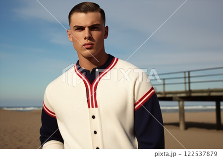 Stylish male model in red and white striped cardigan poses on beach with pier in background, showcasing contemporary men's fashion 122537879