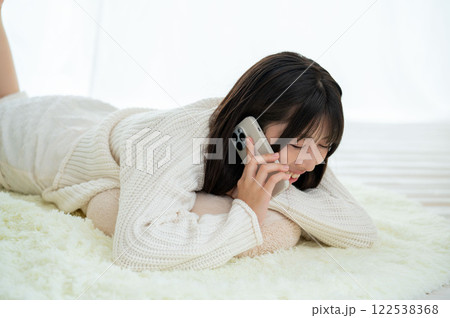うつ伏せに寝てスマホで会話をする日本人女性 122538368