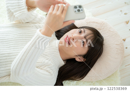 仰向けに寝てスマホを操作する日本人女性 122538369