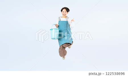 清掃道具を持ってジャンプするエプロンをつけたミドル女性の全身写真 122538696