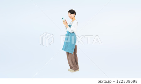 笑顔でスマホを使うエプロンをつけたミドル女性の全身写真 122538698