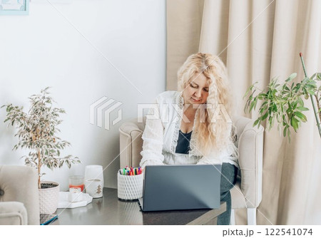 freelancer working on laptop at home, woman with long blonde hair focused on screen, comfortable workspace with plants and decor, concept of modern work, home office, creativity freelancer working on laptop at home, woman with long blonde hair focused on screen, comfortable workspace with plants and decor, concept of modern work, home office, creativity 122541074