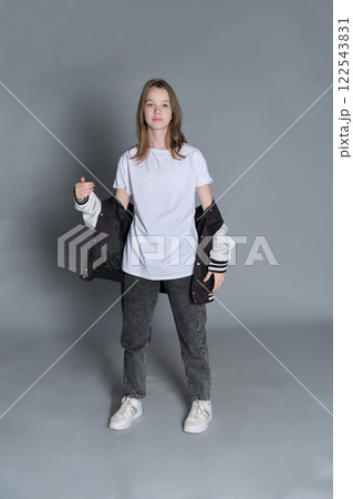 A teenage girl strikes a casual pose, wearing jeans and a varsity jacket over a white shirt. Her outfit represents youthful confidence and the freedom of self-expression in everyday wear. A teenage girl strikes a casual pose, wearing jeans and a varsity jacket over a white shirt. Her outfit represents youthful confidence and the freedom of self-expression in everyday wear. 122543831