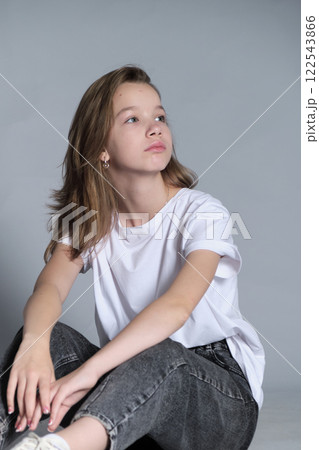 A young girl with a serene expression poses casually, hand resting on her head, against a minimalist backdrop. Calm and reflective moments of youth amidst the hustle of daily life. 122543866