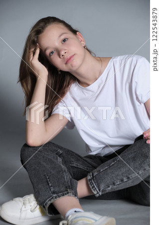 A young girl in jeans and a white t-shirt poses thoughtfully in a studio. This captures the essence of casual style and self-expression in today's youth culture. 122543879