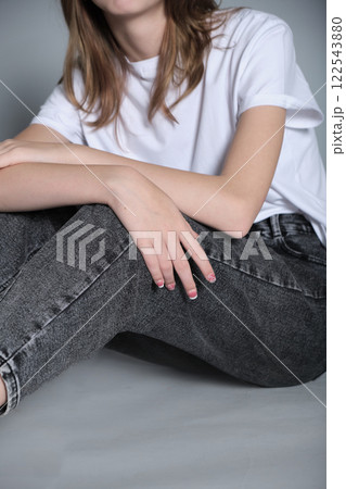 A close-up of a young girl's hand resting on her knee, showcasing her casual style in jeans and a t-shirt. The image highlights simplicity and the natural, laid-back nature of everyday moments. A close-up of a young girl's hand resting on her knee, showcasing her casual style in jeans and a t-shirt. The image highlights simplicity and the natural, laid-back nature of everyday moments. 122543880