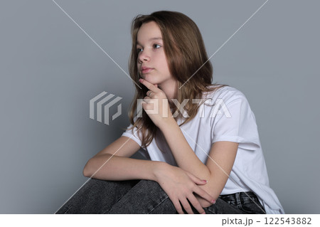 A young girl sits thoughtfully with her hand resting on her chin, wearing casual clothes. This portrait captures the calm introspection and simplicity of modern youth culture. 122543882