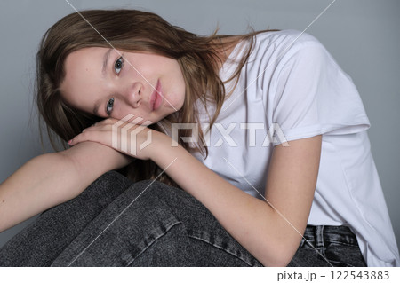 A young girl gently rests her head on her arms, wearing a casual t-shirt and jeans. This soft, relaxed pose reflects a moment of quiet reflection and simplicity in modern youth photography. A young girl gently rests her head on her arms, wearing a casual t-shirt and jeans. This soft, relaxed pose reflects a moment of quiet reflection and simplicity in modern youth photography. 122543883
