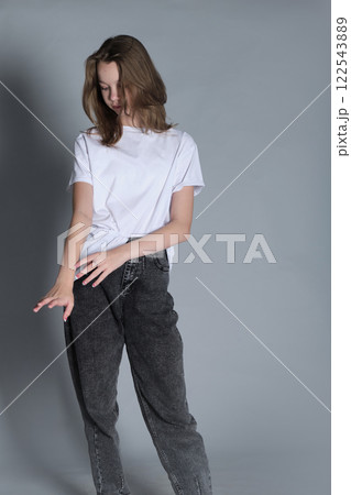A young girl dressed in a white t-shirt and jeans looks down while standing calmly. This portrait emphasizes a quiet moment of reflection, showcasing natural beauty and minimalism. A young girl dressed in a white t-shirt and jeans looks down while standing calmly. This portrait emphasizes a quiet moment of reflection, showcasing natural beauty and minimalism. 122543889