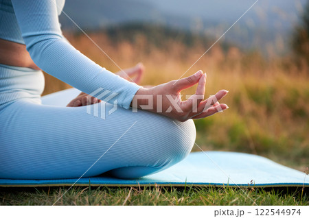 Close up of woman's hands on dawn background in the evening. Woman doing yoga exercise and meditating during sunset in mountains 122544974