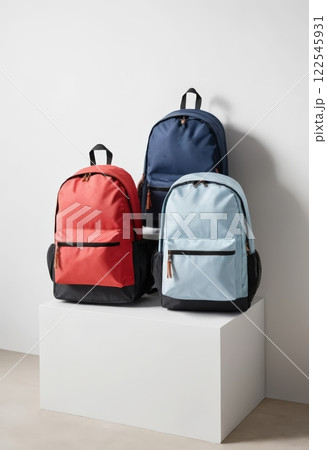 A frontal view of three backpacks in red, navy, and soft blue, displaying modern design and functionality. Ideal for fashion retailers or outdoor gear enthusiasts. A frontal view of three backpacks in red, navy, and soft blue, displaying modern design and functionality. Ideal for fashion retailers or outdoor gear enthusiasts. 122545931