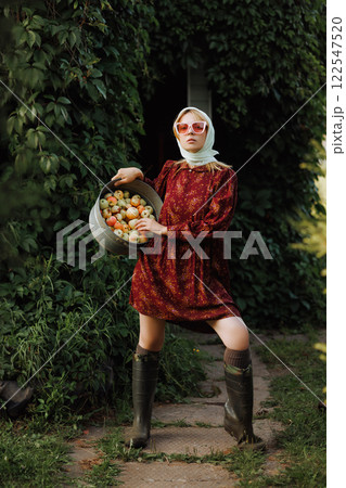 A fashionable woman in a red dress is holding a bucket full of apples 122547520