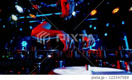 DJ Mixing Music on Turntable in Nightclub with Vibrant Lights 122547569