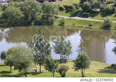 Lush greenery of trees and lawns around the pond in the park, urban landscape park. Lush greenery of trees and lawns around the pond in the park, urban landscape park. 122548083