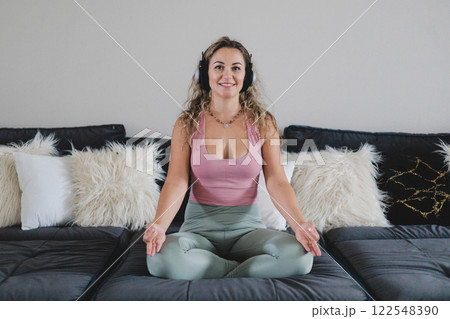 Smiling yoga woman in headphones sitting in lotus position on couch enjoy meditation Smiling yoga woman in headphones sitting in lotus position on couch enjoy meditation 122548390