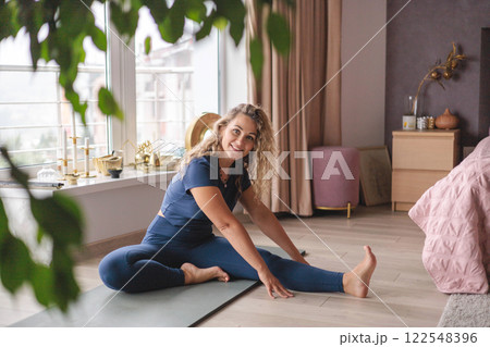 Yoga woman stretching body with raising hand sitting on mat at home panorama window Yoga woman stretching body with raising hand sitting on mat at home panorama window 122548396