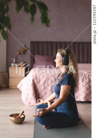 Smiling yoga woman meditation in lotus position listening music use headphones at home 122548397