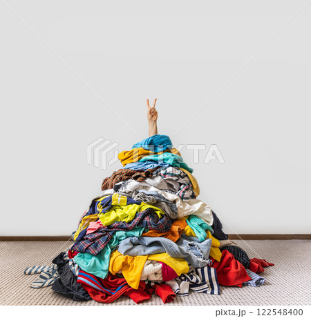 Unrecognizable human raises arm reaches out heap of colorful unfolded clothes busy doing wardrobe Unrecognizable human raises arm reaches out heap of colorful unfolded clothes busy doing wardrobe 122548400