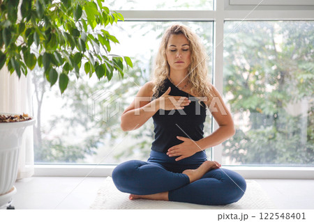 Woman yoga meditation sitting in lotus position near panorama window with houseplant at home Woman yoga meditation sitting in lotus position near panorama window with houseplant at home 122548401