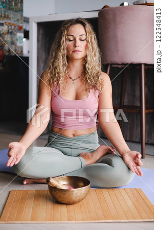 Yoga woman meditation in lotus pose with signing bowl sitting on mat at home Yoga woman meditation in lotus pose with signing bowl sitting on mat at home 122548413