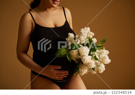 Pregnant woman holding flowers celebrating motherhood on a warm tonal background 122548514