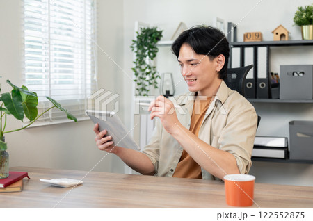 A creative Asian businessman sits at his desk in the office, designing artwork on his digital tablet A creative Asian businessman sits at his desk in the office, designing artwork on his digital tablet 122552875