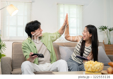 A cheerful couple give a high five to each other to celebrate after winning a game on their phones. 122553116