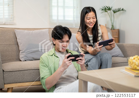 An overjoyed, happy Asian couple enjoys playing a racing game on their smartphones together. An overjoyed, happy Asian couple enjoys playing a racing game on their smartphones together. 122553117
