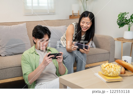 An overjoyed, happy Asian couple enjoys playing a racing game on their smartphones together. An overjoyed, happy Asian couple enjoys playing a racing game on their smartphones together. 122553118