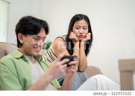 A moody Asian girl sits in the living room, feeling ignored by her boyfriend. A moody Asian girl sits in the living room, feeling ignored by her boyfriend. 122553122
