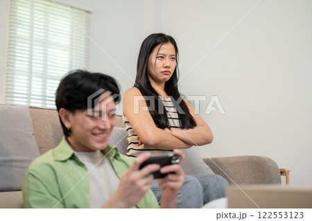 A moody girl sits in the living room, feeling ignored by her boyfriend as he plays a mobile game. 122553123
