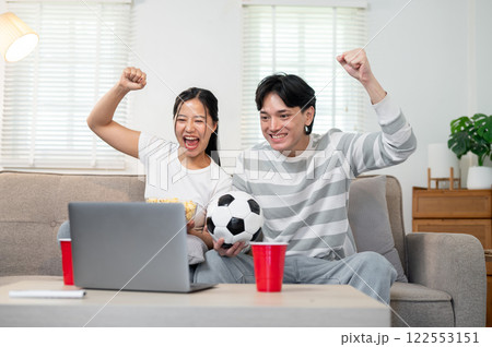 A happy Asian couple supporting their favorite team and enjoying watching the match together at home A happy Asian couple supporting their favorite team and enjoying watching the match together at home 122553151