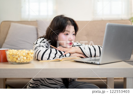 A tired Asian female university student is feeling bored from her online lecture, studying at home. 122553403