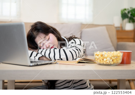 An Asian female student feeling exhausted from her online lecture, is taking a nap at a coffee table 122553404