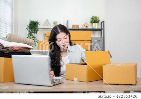 A beautiful Asian female business owner is checking and packing items for her customers. 122553420