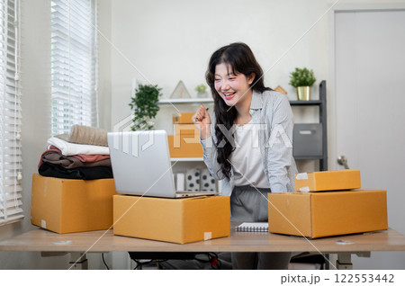 Smiling Asian female business owner is happy with the large number of orders, working in her office. Smiling Asian female business owner is happy with the large number of orders, working in her office. 122553442
