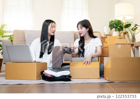 Two Asian female online shop owners are working in the living room, discussing while packing goodies 122553733
